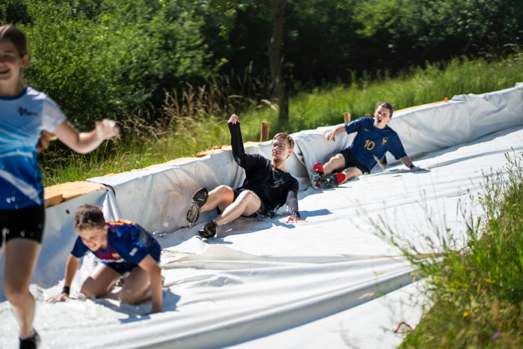 Teilnehmende rutschen auf der Wasserbahn beim Dreck Race