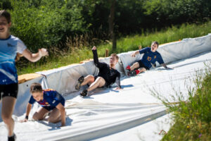 Teilnehmende rutschen auf der Wasserbahn beim Dreck Race während des J-Camp 2025