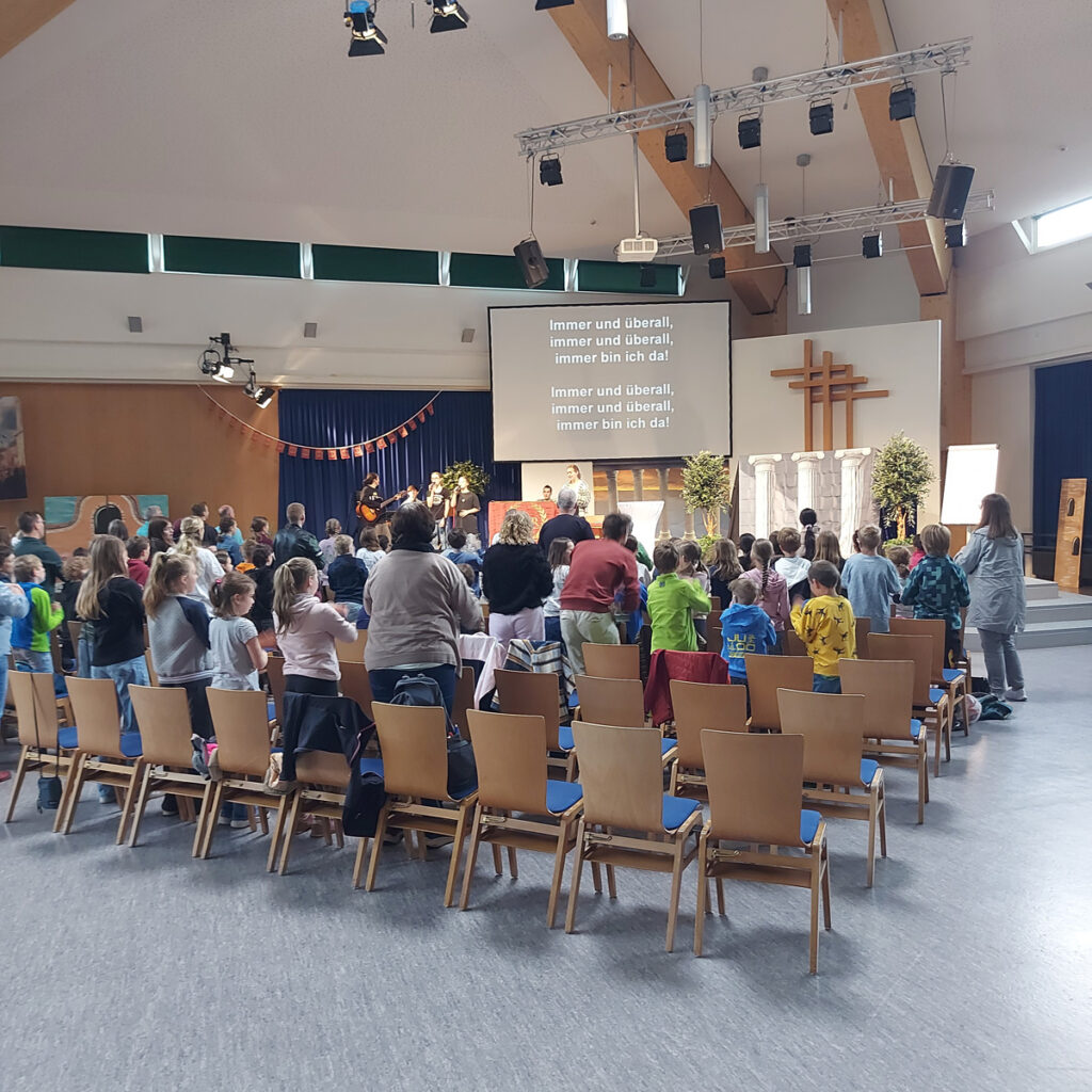 Blick von hinten auf die Kinder, die beim Jungschartag 2026 "Geheimzeichen Fisch" in der Evangeliumshalle vor der Bühne auf Stühlen sitzen